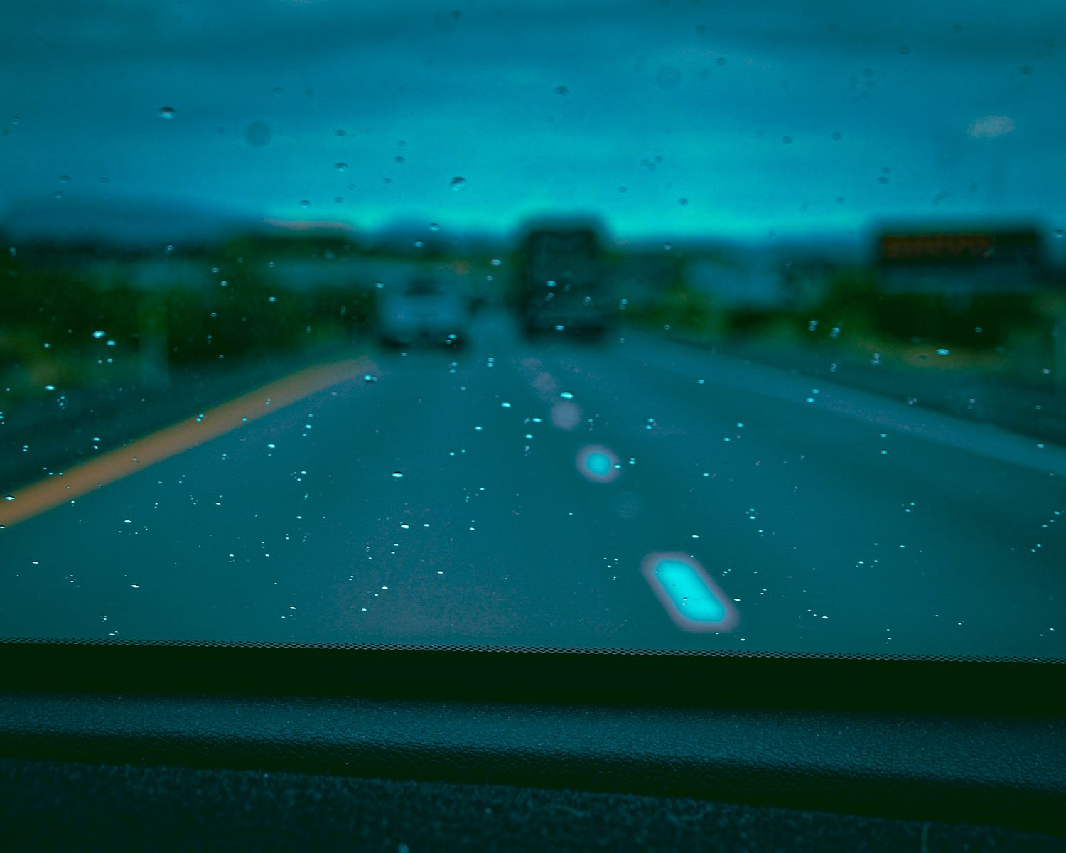 Rainy windshield view of road with teal color toning.