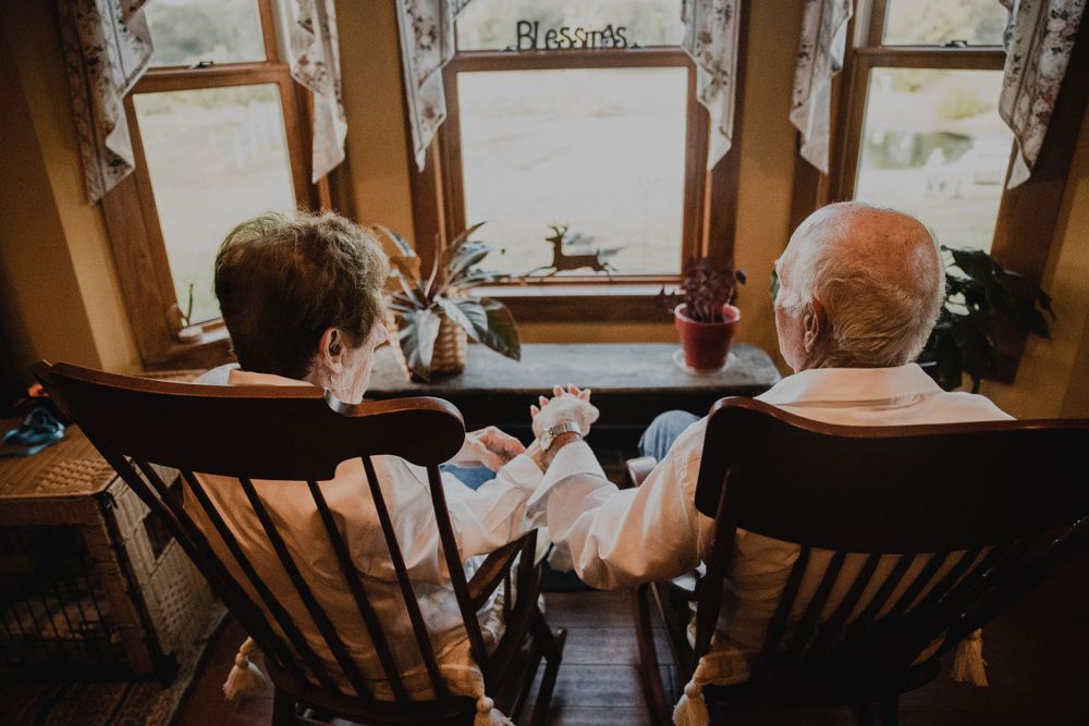 Two people sitting in rocking chairs by a window looking out at winter scenery.