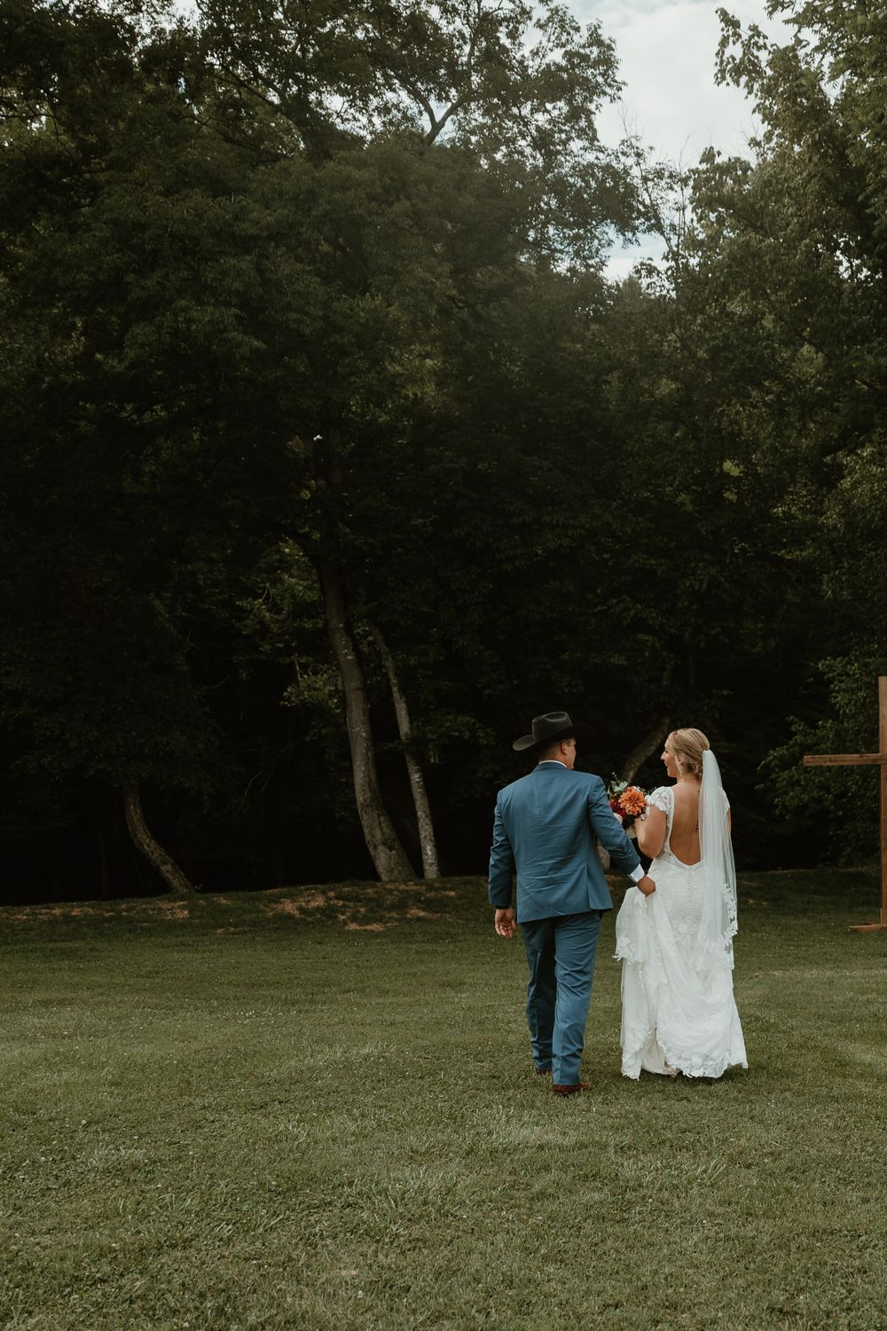 Wedding couple walking hand in hand through garden path in formal attire.