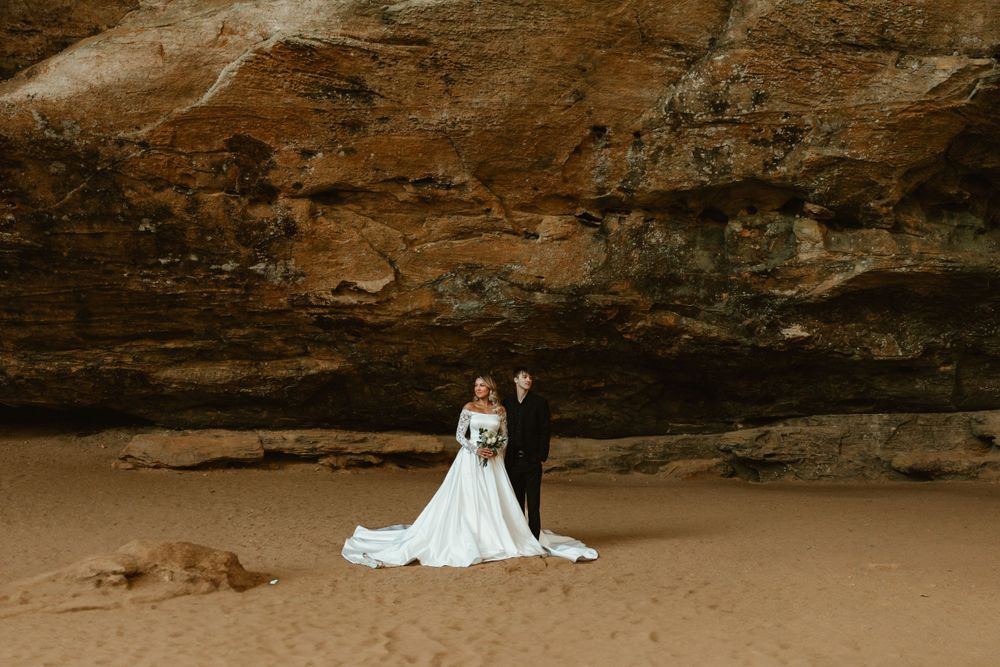 Wedding couple photographed against dramatic rocky cave backdrop.