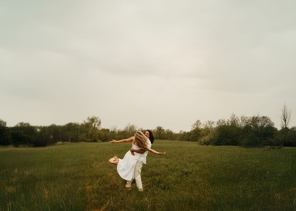 A person in white flowing fabric dances gracefully across a green meadow at sunset.