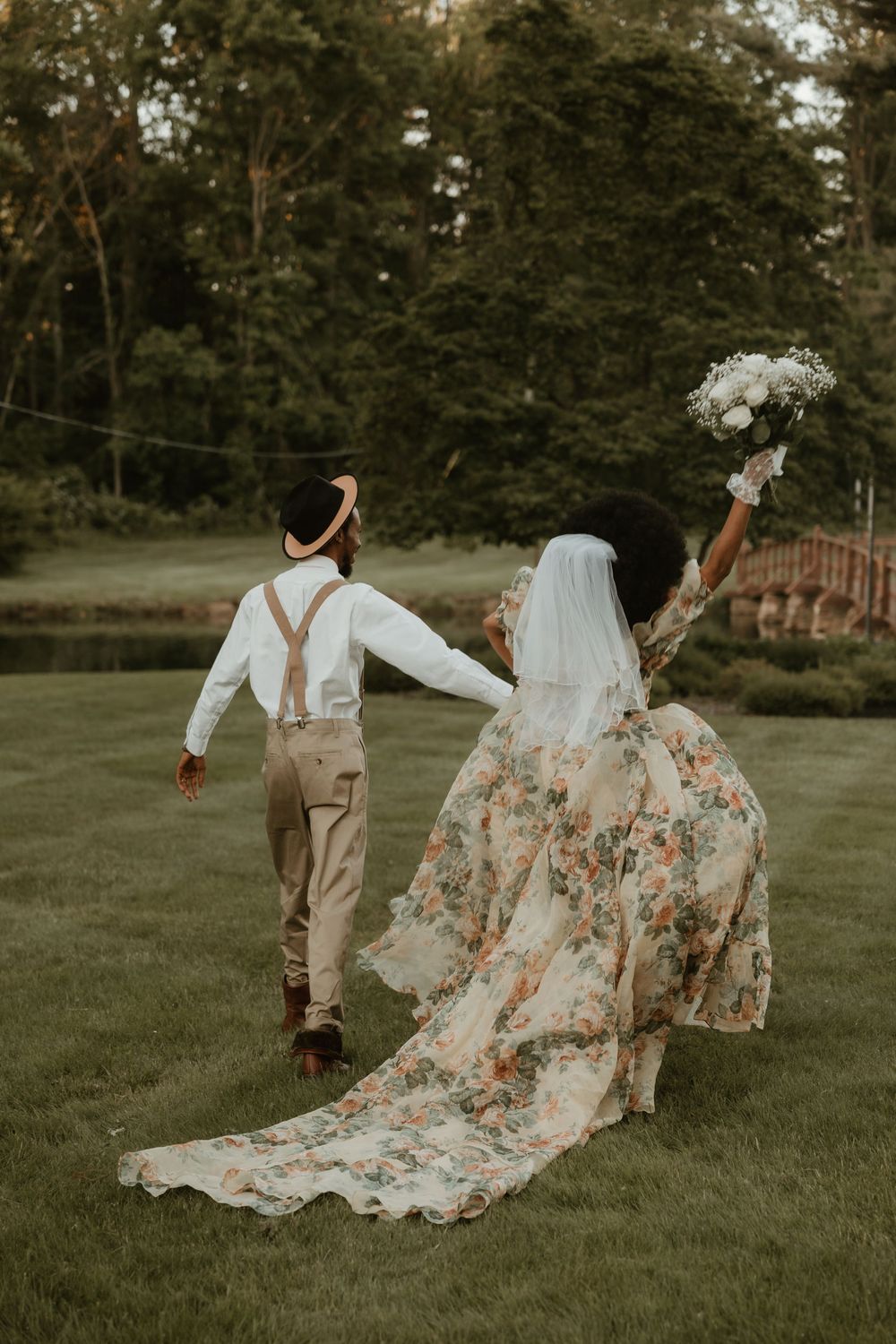 A couple in wedding attire dances playfully on a grassy lawn at sunset, with the bride's floral dress flowing elegantly.