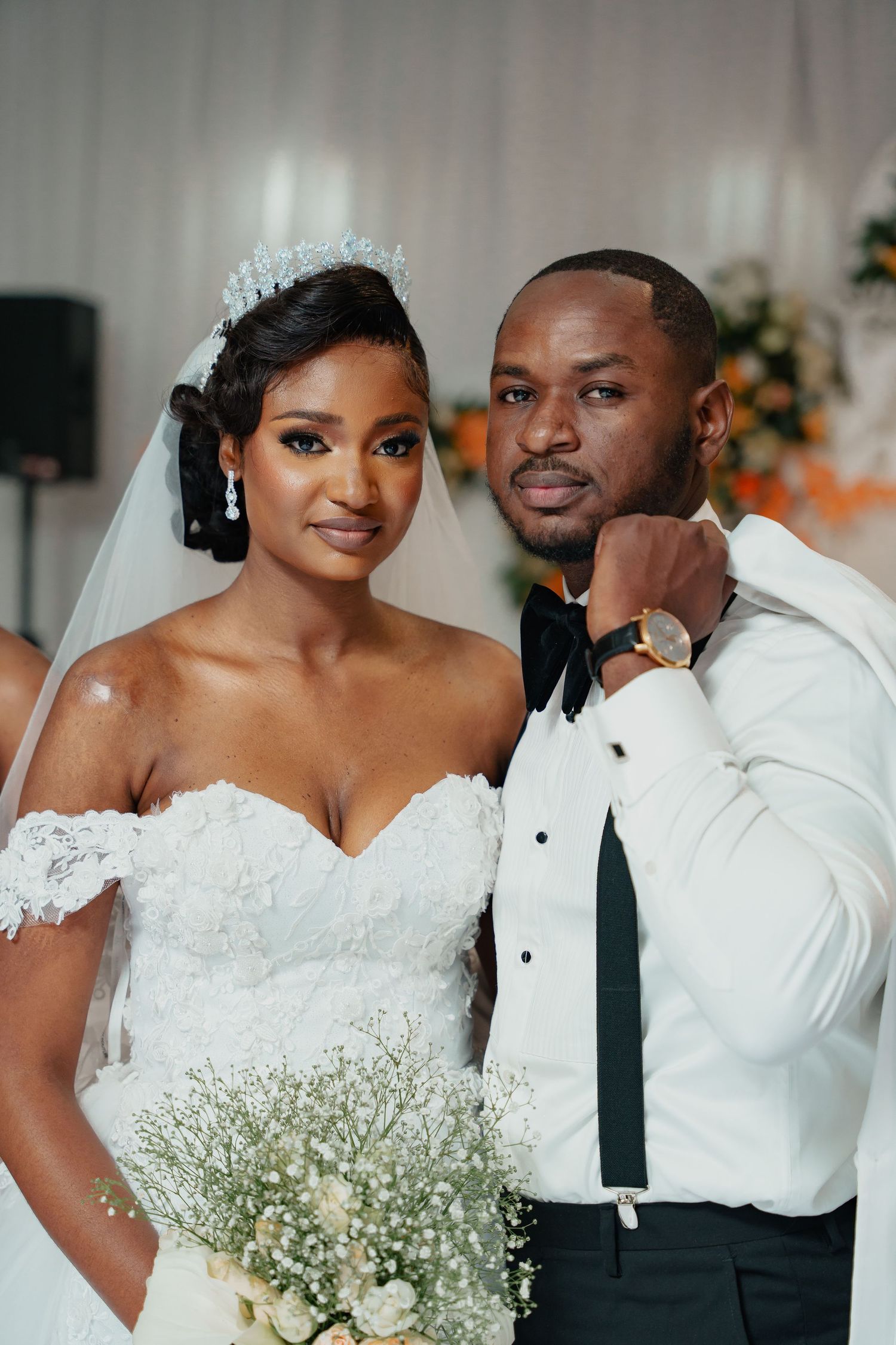 Wedding portrait of bride in off-shoulder gown and groom in white tuxedo jacket.