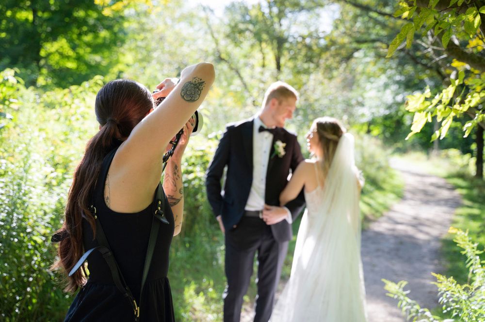 Wedding photographer capturing a couple on a sunlit forest path during their outdoor photo session in the summertime.