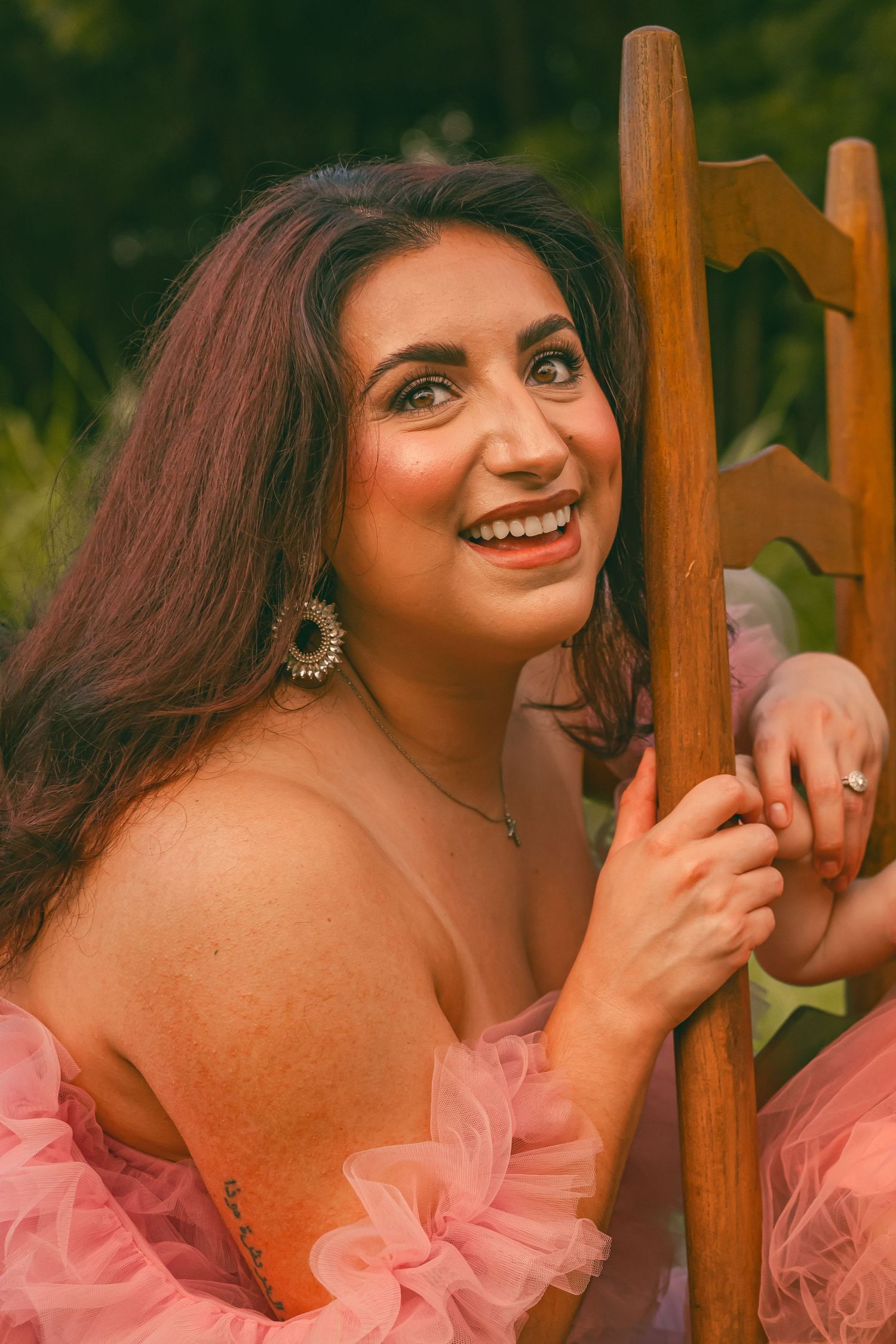 Portrait series against wooden fence wearing pink flowing top and statement earrings.