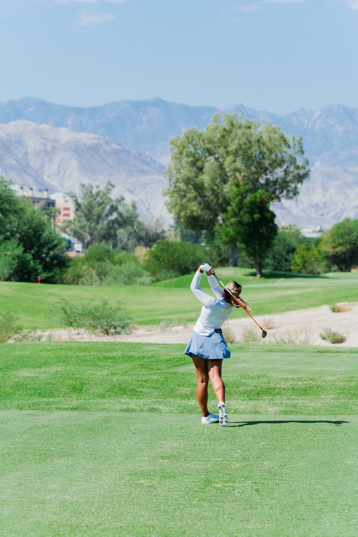 A golfer takes a swing on a scenic golf course with mountains and green trees in the background.
