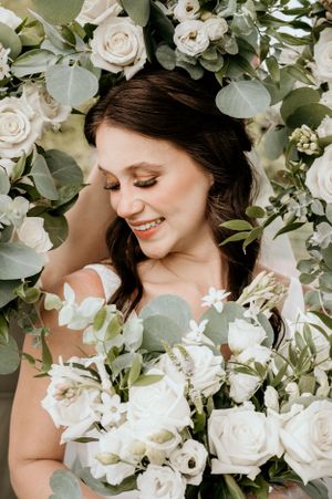 Bride smiles while surrounded by a ring of her bridesmaids white flower bouquets.