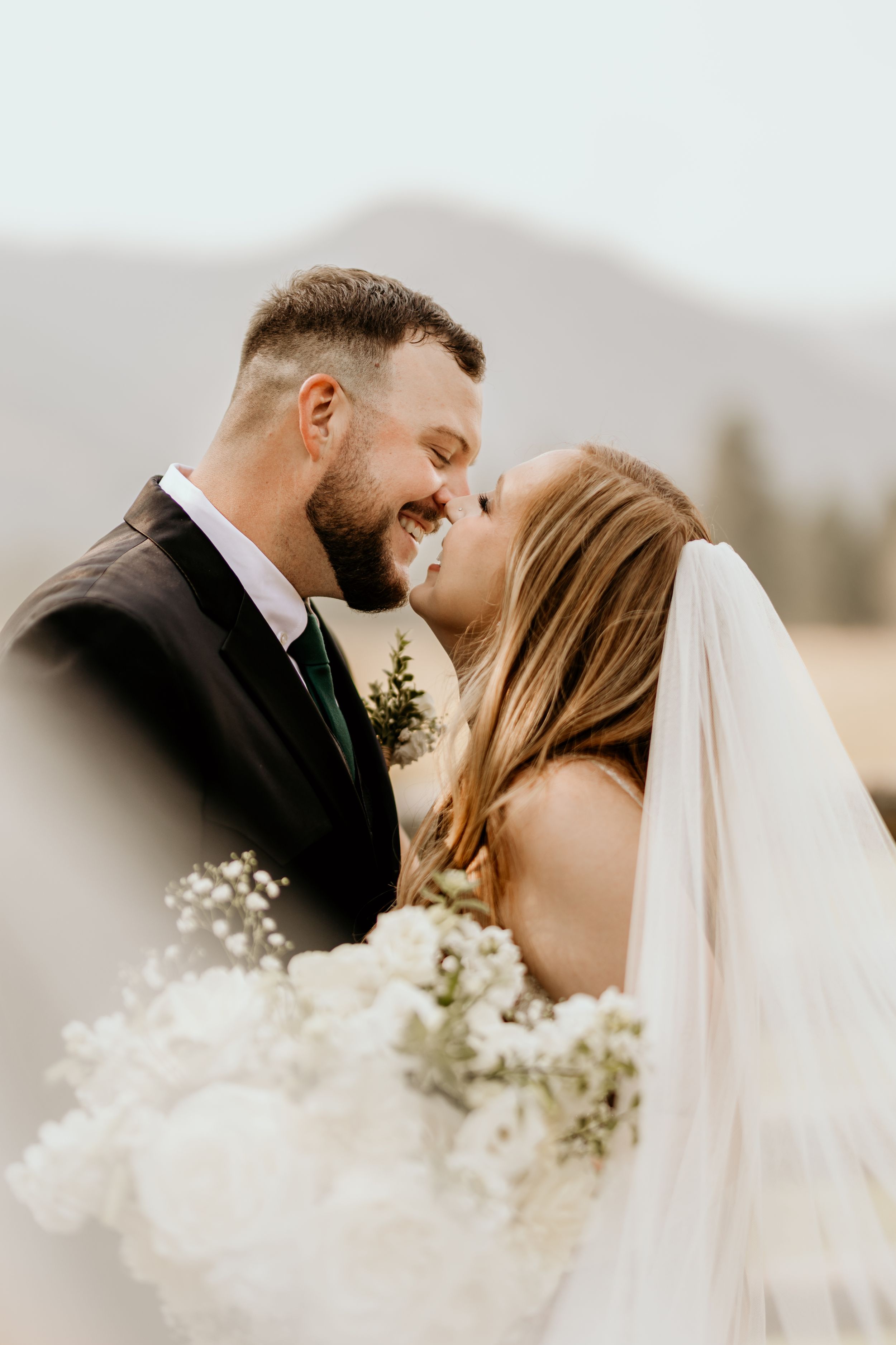A bride and groom share a joyful, intimate moment outdoors, with their foreheads touching and smiles on their faces.