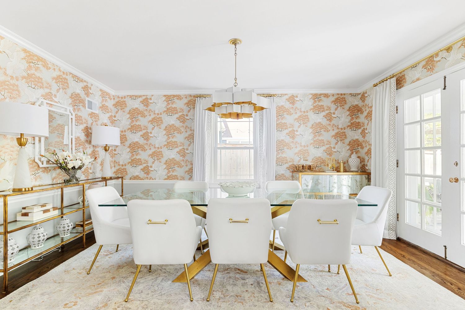 Cream and gold dining room with unique pendant chandelier and bold patterned wallpaper.