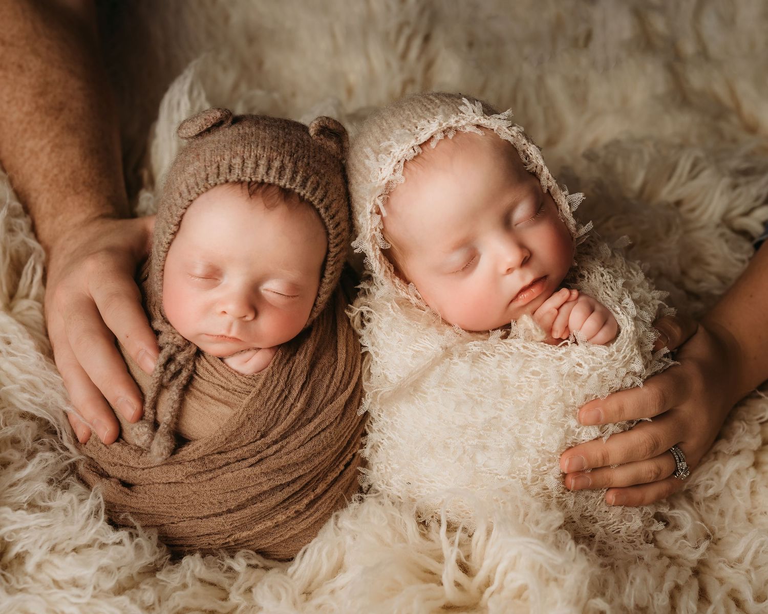Sleeping twin newborns swaddled in brown and cream wraps with knit bonnets in studio photo.