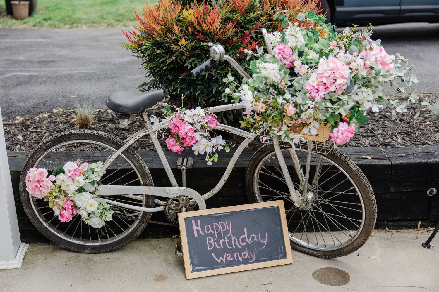 Vintage bicycle decorated with pink and white flowers next to a chalkboard sign for wedding decor.