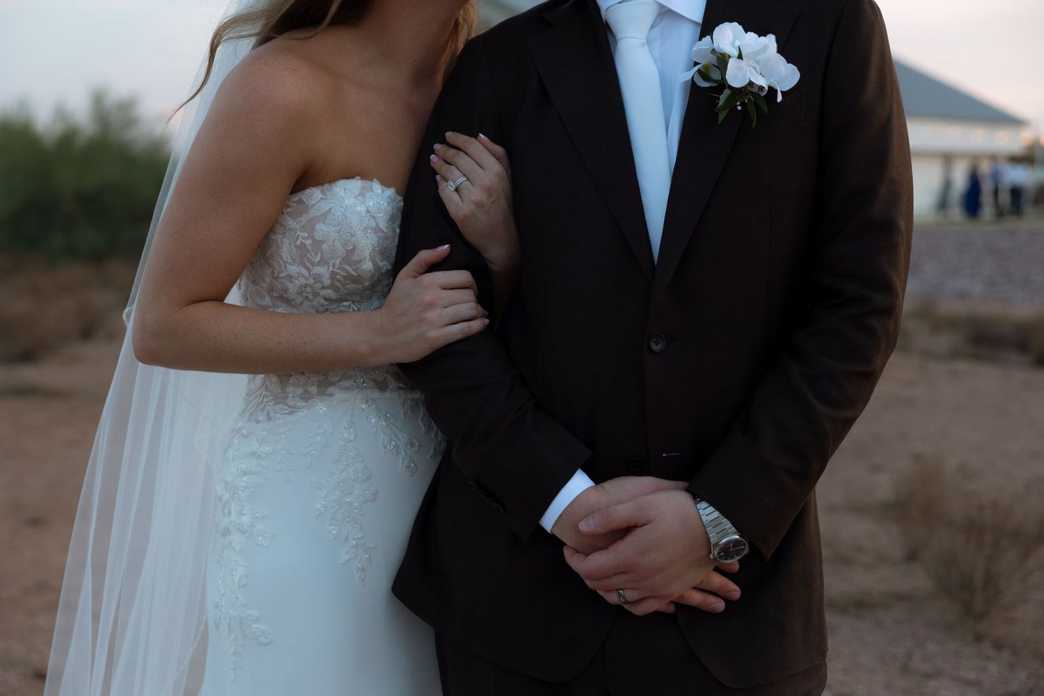 A close-up shot of a couple in wedding attire embracing outdoors at dusk, with a black suit and white dress.