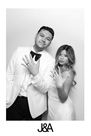 Black and white portrait photo of a couple in elegant white attire posing playfully with hand gestures.