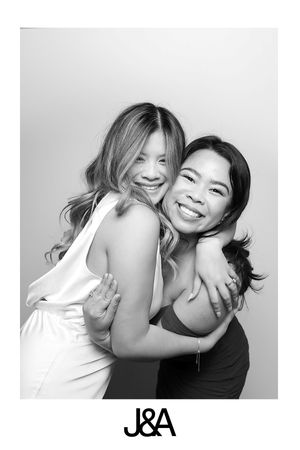 Two women in black and white photo hugging and smiling warmly at camera with J&A text at bottom.