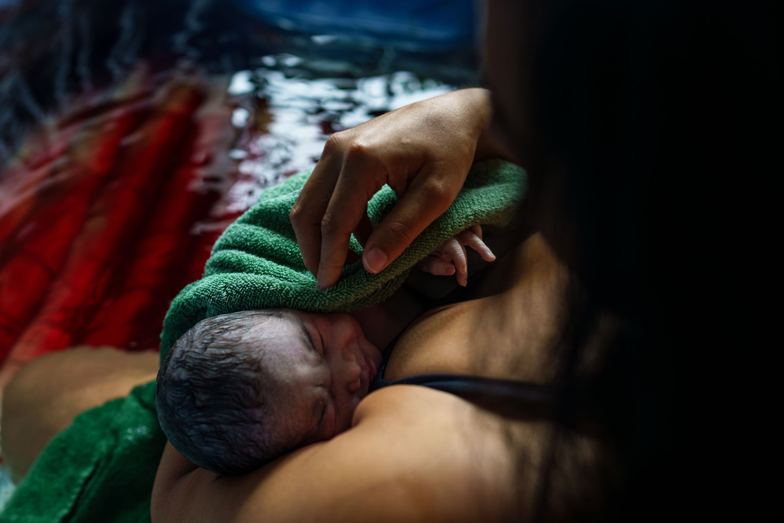 Newborn baby being gently cleaned with green cloth after birth.