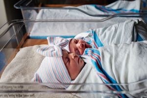 Newborn baby wrapped in striped blanket sleeping peacefully in hospital bassinet after birth.