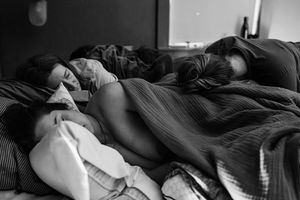 Black and white photo of two people sleeping peacefully together in bed covered with cozy blankets.