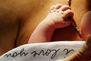 Close-up of a newborn baby's tiny feet resting on a blanket with 'i love you' script near a mother's tattoo.