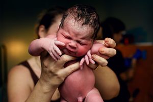 Newborn baby held up immediately after birth, crying with umbilical cord still attached.