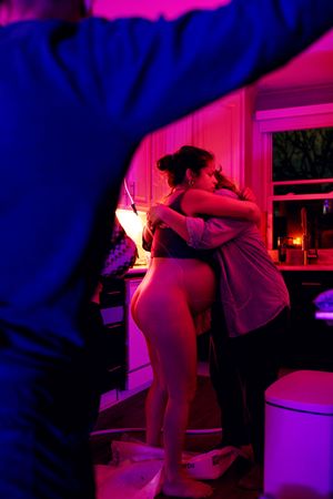 Two people embracing in a kitchen bathed in purple and pink neon lights.