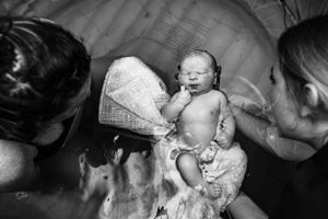 A tender moment captured in black and white as a newborn is lifted from the birthing pool.