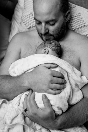 Intimate skin-to-skin bonding moment with a newborn wrapped in white cloth.