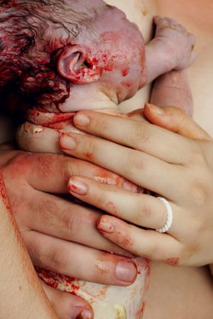 Mother holding her newborn baby covered in vernix immediately after birth, with hands showing a wedding ring.