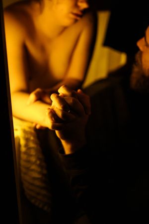 Two people holding hands in warm golden light, an intimate romantic moment captured in moody low-key lighting.