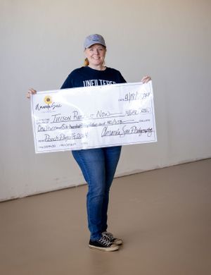 Someone holds up a large promotional check against a plain wall while wearing casual attire.
Photographer Tucson Giving back