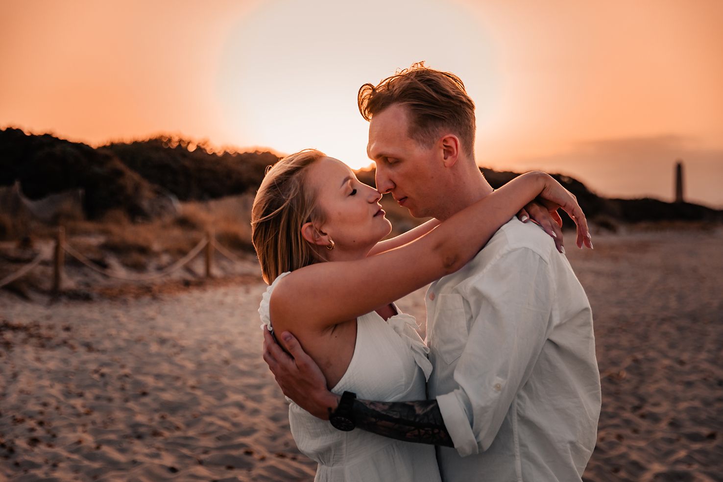 Romantic close up of a woman wrapping her arms around a mans neck on a sandy beach site.