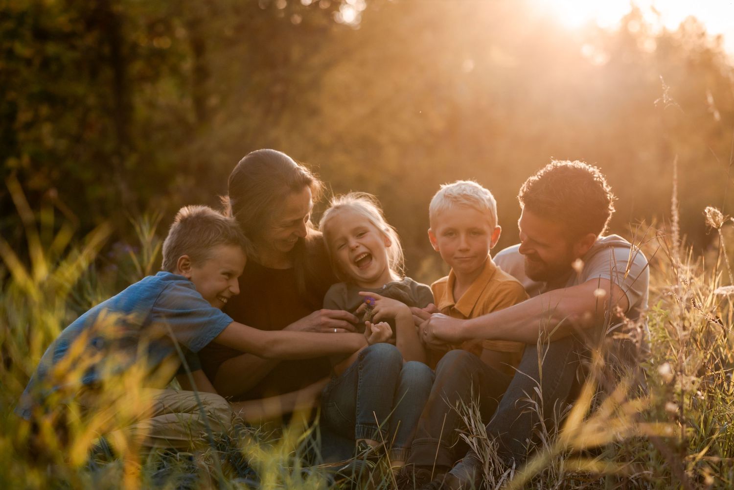 A group huddles together in a field at sunset sharing a joyful moment in golden light.