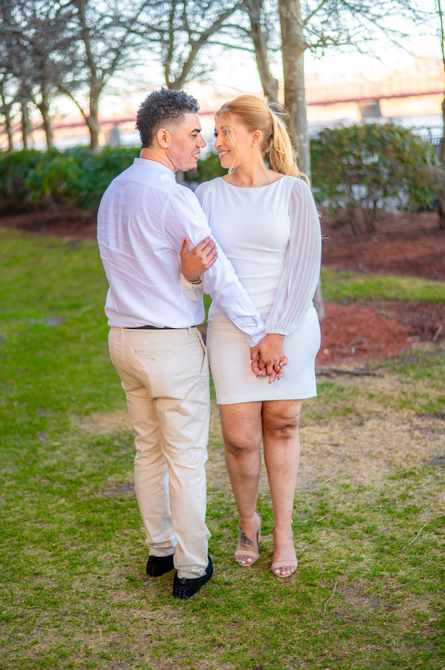 A loving couple in white attire sharing an intimate moment in a garden setting.