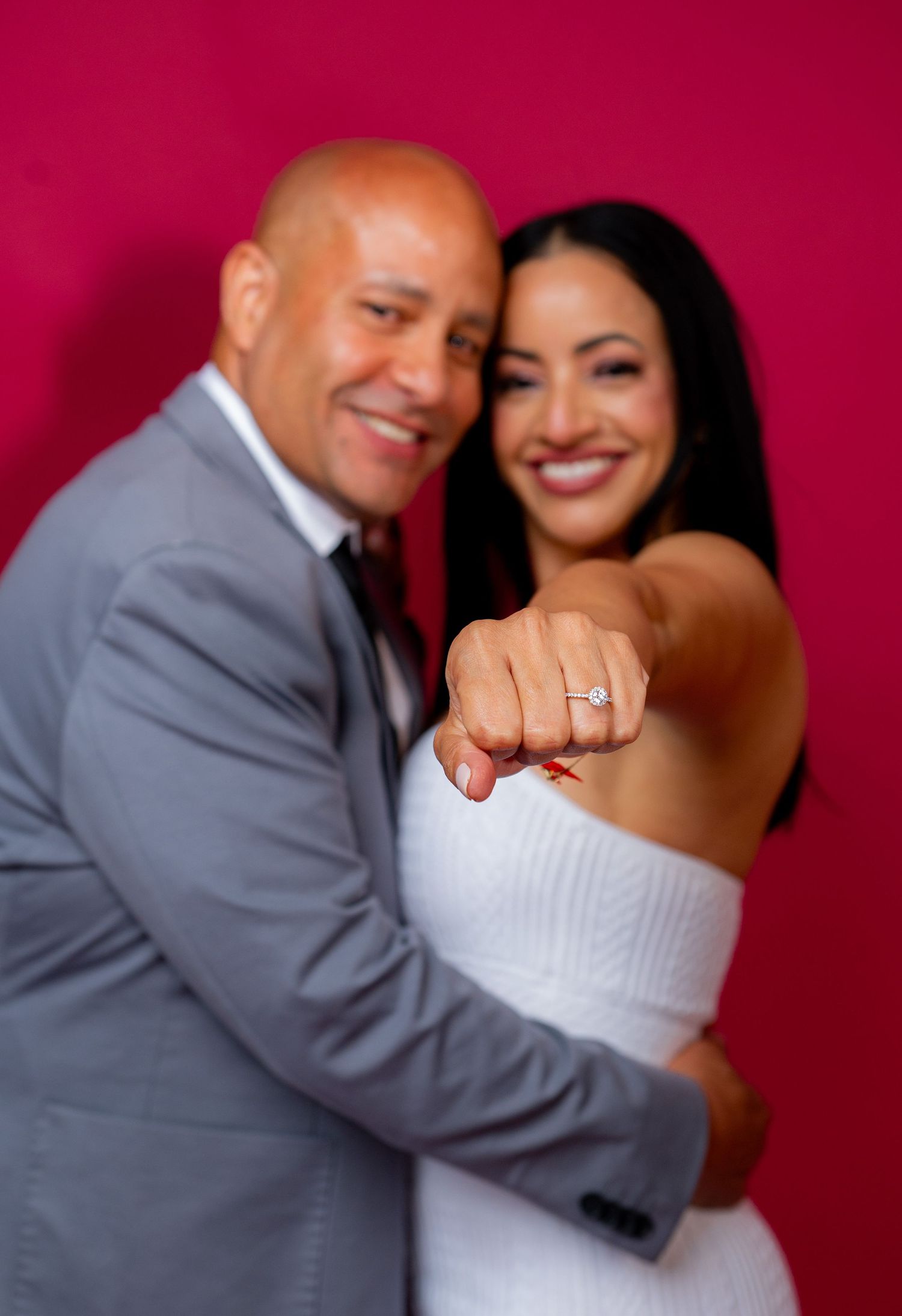 Intimate couples photography with white dress and grey suit against crimson backdrop.