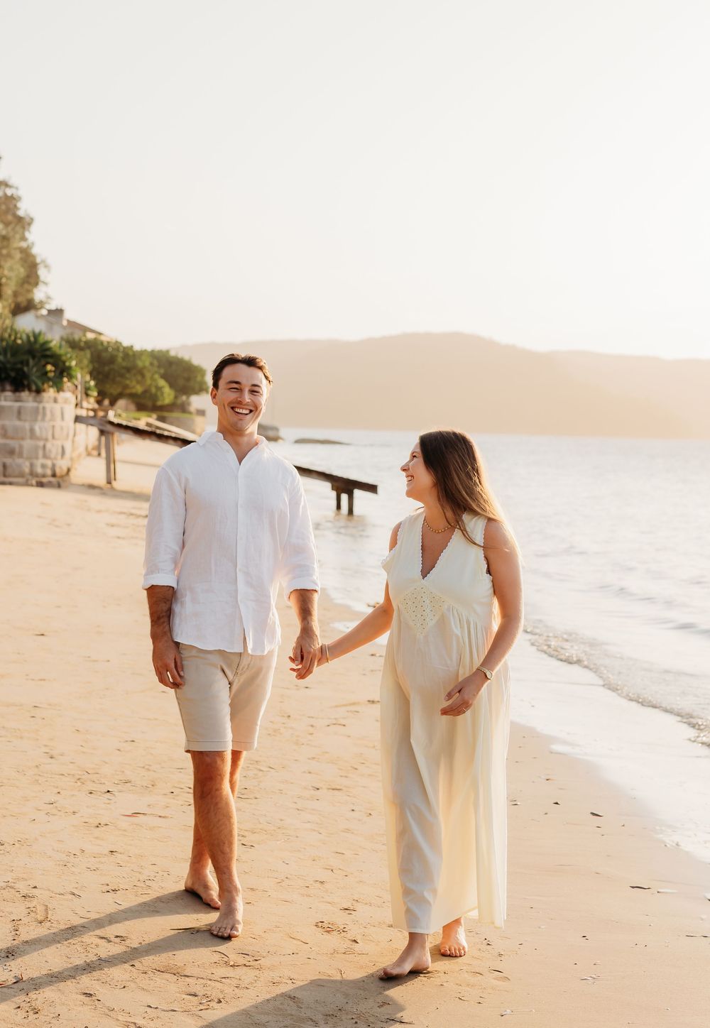 Expecting couple walking hand in hand along the beach at sunset