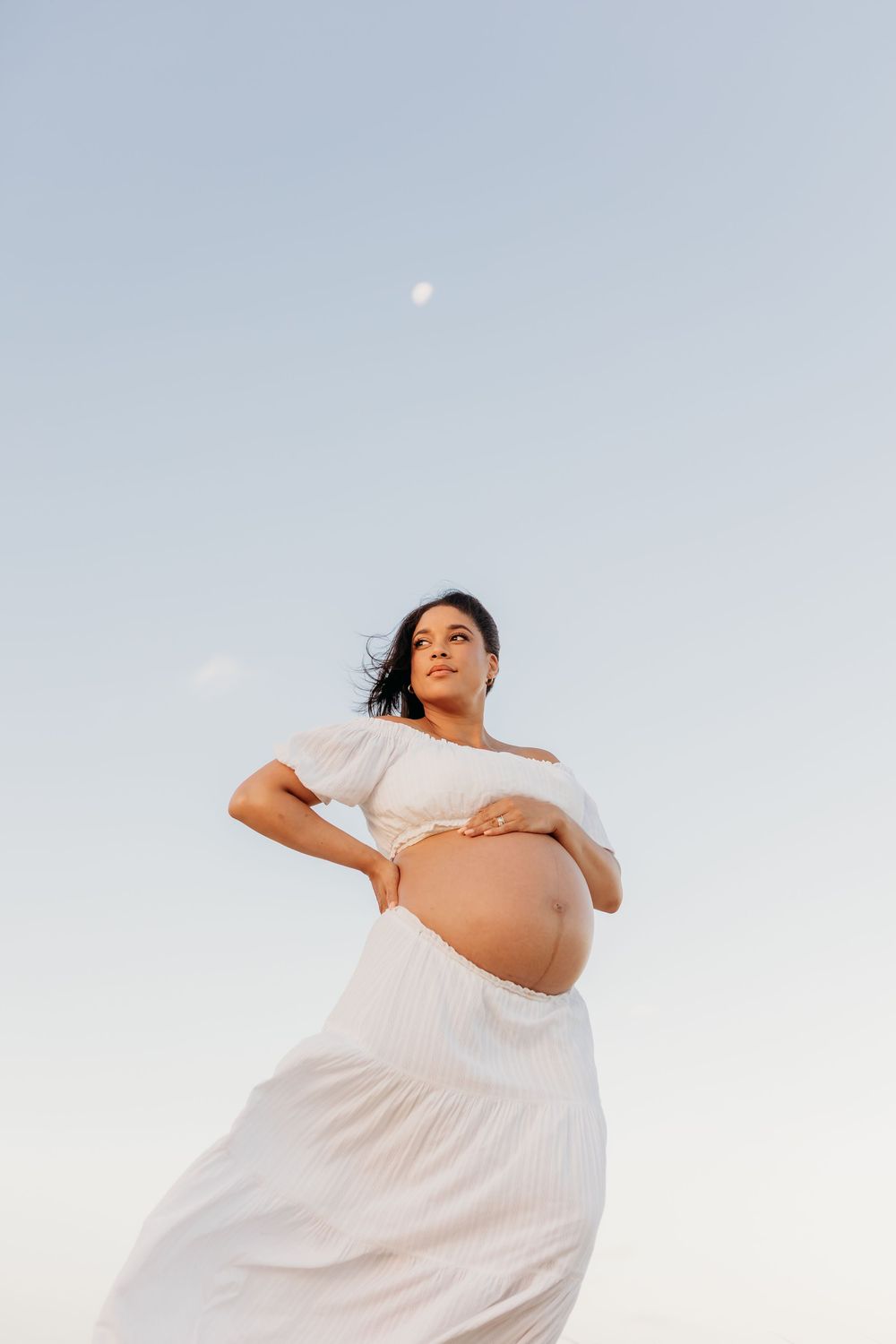 Maternity portrait of woman in white dress cradling her bump, Sunshine Coast