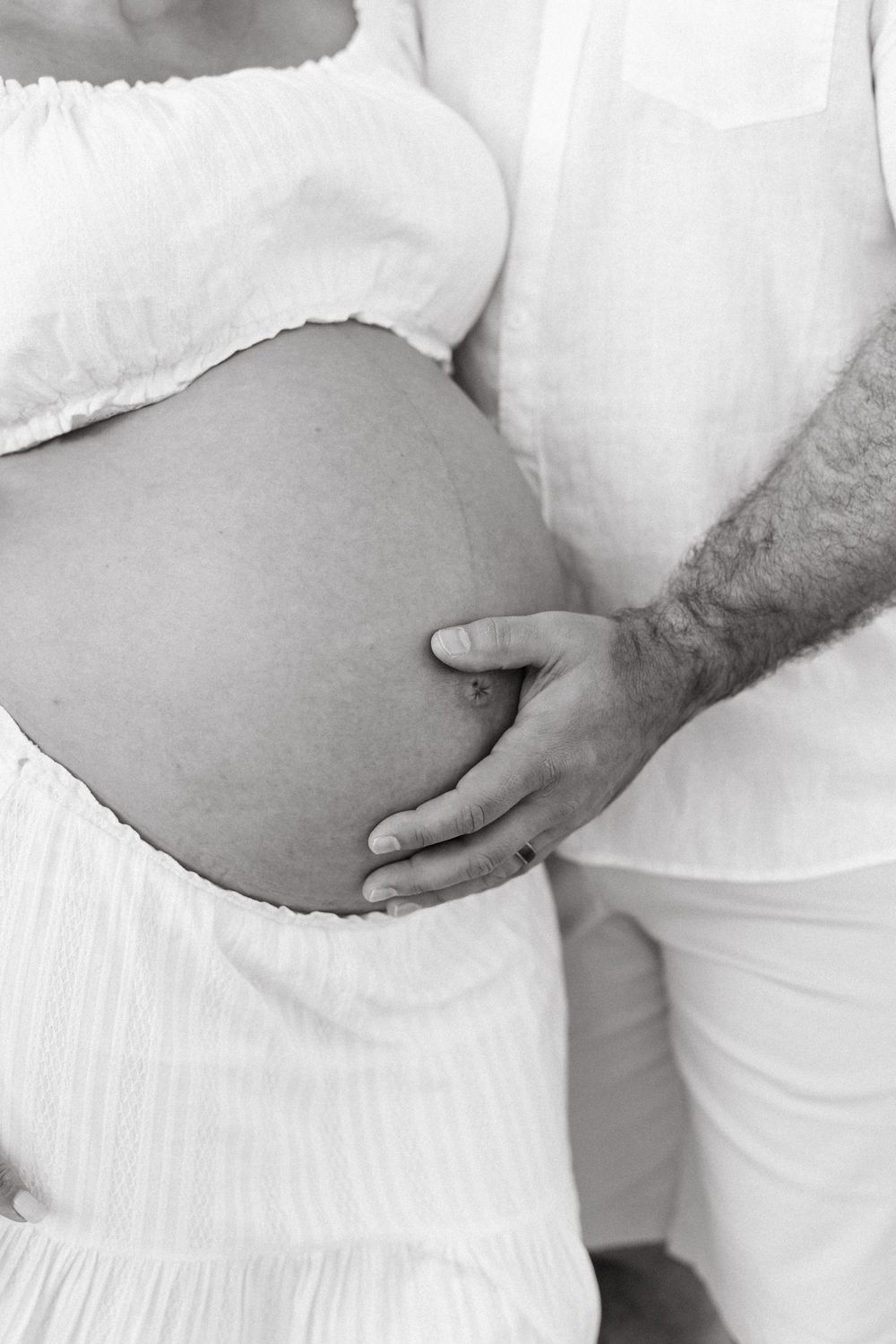 Black and white close-up of couple's hands on pregnant belly, maternity session