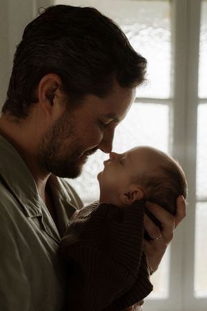 A silhouetted parent holds and gazes lovingly at their newborn baby near a sunlit window.