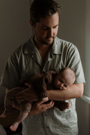 A tender moment as a caregiver in a light blue shirt cradles a sleeping baby wrapped in a brown blanket.