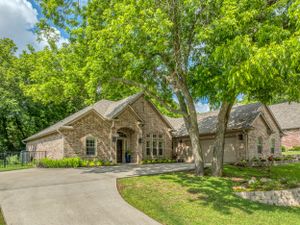 Sprawling stone ranch house with circular driveway nestled among mature trees.
