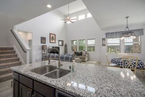 Open concept kitchen and living area with granite countertops, vaulted ceiling, and modern finishes.