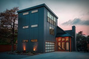 Contemporary blue modern house with glass garage door illuminated at dusk.