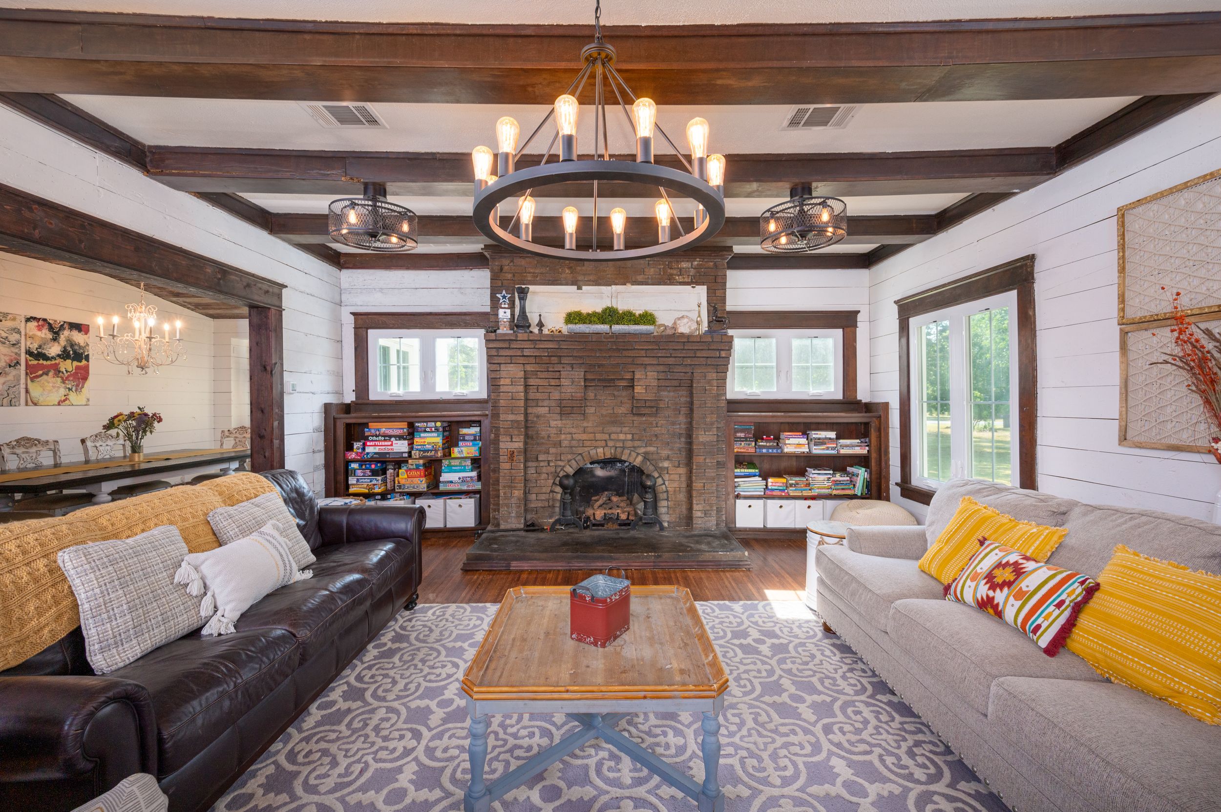 Rustic living room with exposed wooden beams, stone fireplace, and circular chandelier.