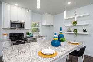 Modern white kitchen with granite countertops, stainless steel appliances, and bright blue accent decor.