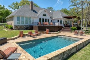 Modern home with elevated deck and pool featuring stone coping and loungers.