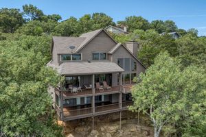 Multi-level luxury home with expansive deck nestled among trees on a wooded hillside property.