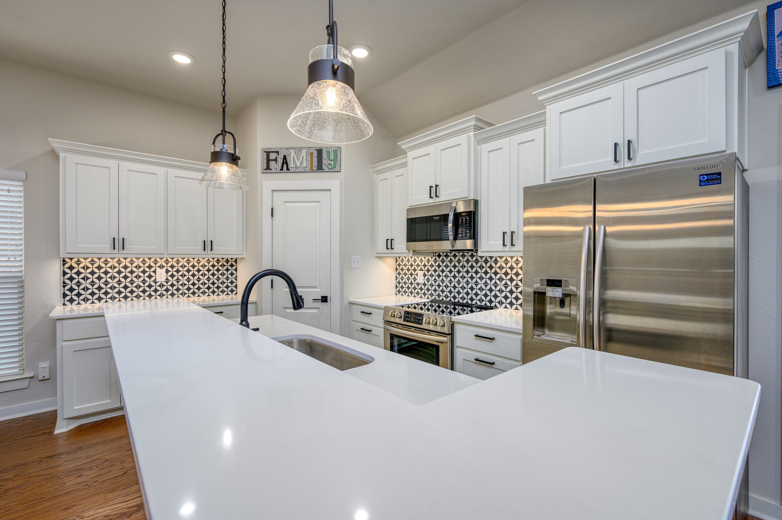 Modern white kitchen with stainless steel appliances and pendant lighting over center island.