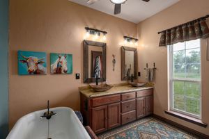 Elegant master bathroom featuring a freestanding tub, wooden vanity, turquoise wall art, and large window with natural light.