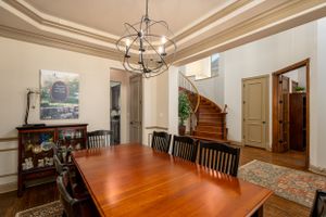 Elegant dining room featuring wood table, traditional chairs, and orbital chandelier with curved staircase in background.