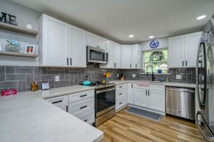 Modern white kitchen with stainless appliances, gray backsplash, and wood-look flooring.