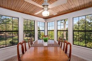 Sun-filled dining room with wood plank ceiling and large windows offering scenic views of nature.